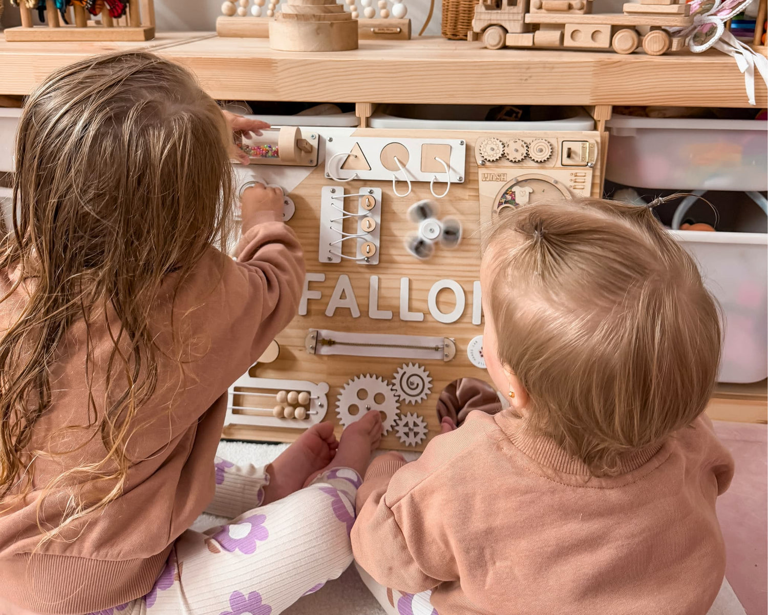 Two toddlers playing with a wooden busy board in an elegant playroom.